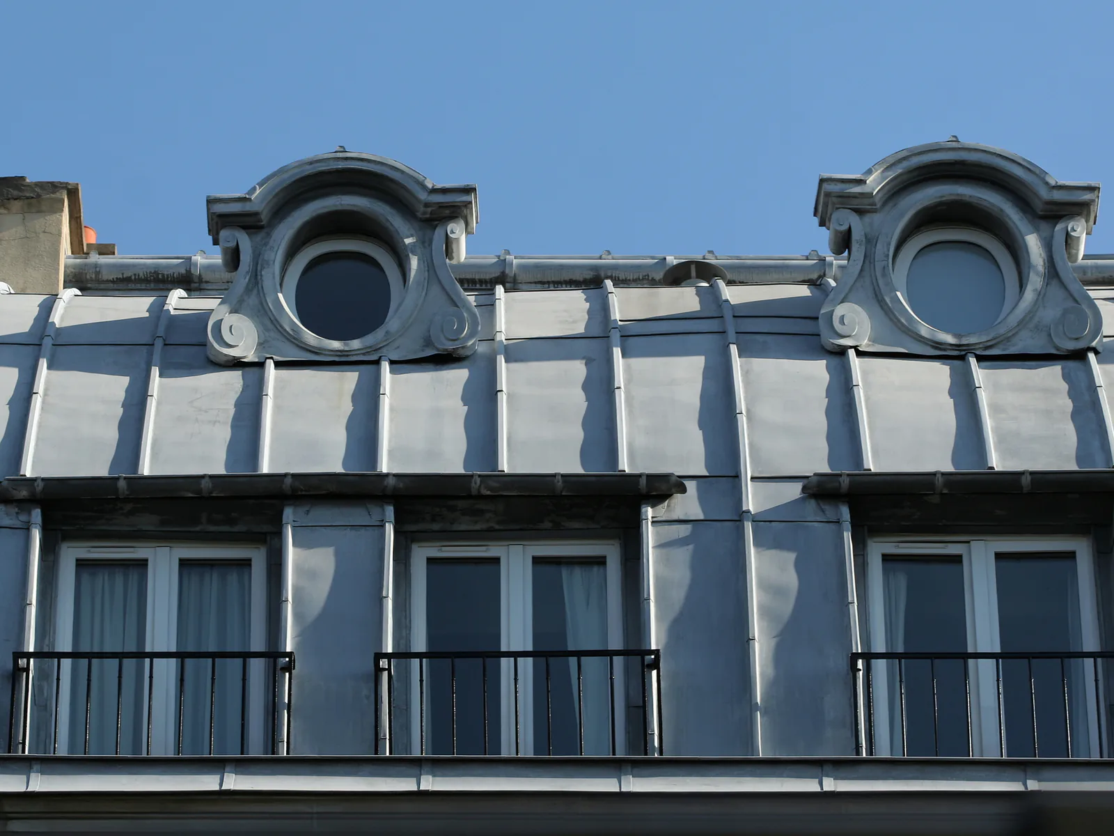 Toiture parisienne en zinc à tasseaux, feuilles gris bleuté et lucarnes en œil-de-bœuf