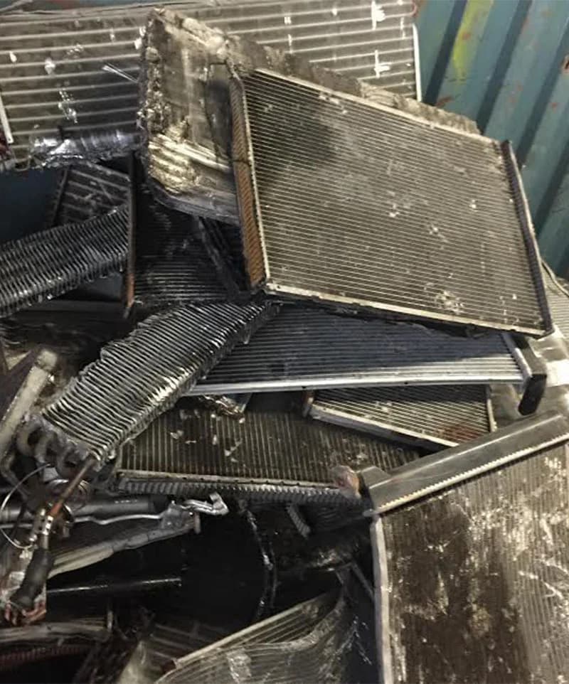 Tas de radiateurs et condenseurs automobiles déposés, faisceaux gris et durites encore en place